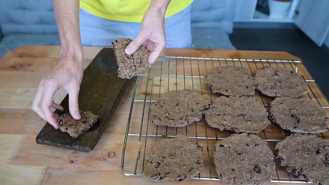 Person breaking homemade buckwheat raisin crispbread above cooling rack in kitchen video Full HD