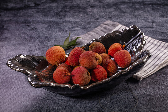 Fresh ripe red lychee fruits in decorative black bowl on dark textured background
