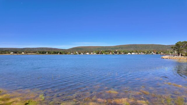 Slow motion footage view across the calm waters of Annapolis Basin in Annapolis Royal Nova Scotia Canada with distant shoreline homes rolling hills and clear blue skies creating a peaceful maritime