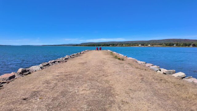 Slow motion footage of scenic rocky breakwater stretching into the waters of Annapolis Basin at Annapolis Royal Nova Scotia Canada with two red chairs at the end of the jetty