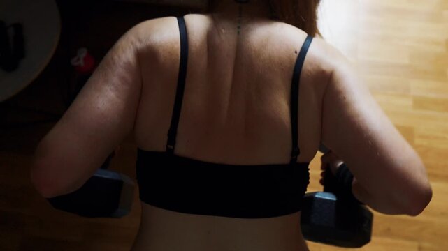 Woman's back and shoulders showcasing muscle activation while performing dumbbell rows during a home workout, embodying concepts of fitness, strength, healthy lifestyle, and female empowerment