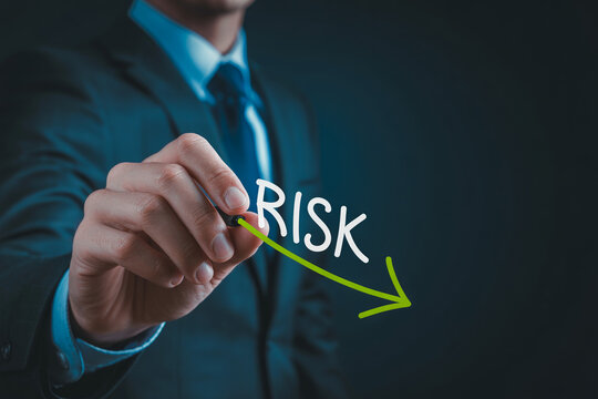 Business person hand writing risk word with green arrow showing downward trend.