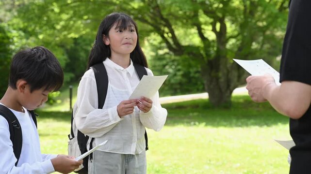 新緑の湖畔で地図を見ながら遠くを指差して発見を喜ぶ小学生グループ