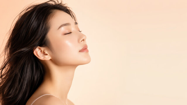 Young woman side profile with dewy glowing skin on peach background