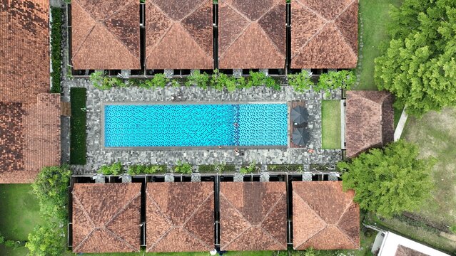 Aerial view of a luxury resort with a blue swimming pool and traditional brown tiled roofs surrounded by lush greenery in Borobudur, Central Java, Indonesia.