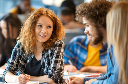 University students engaged in group study during a classroom session, young adults discussing lecture tasks while writing notes and preparing for exams together. 