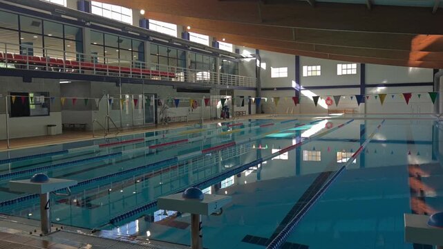 Wide angle horizontal video of indoor swimming pool with maintenance worker cleaning floor
