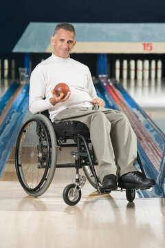 Portrait of a mature man with a Spinal Cord Injury holding a bowling ball and smiling
