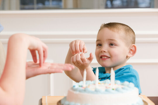 Boy signing the word 'Cake' in American sign language sitting in front of a birthday cake