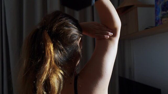 Woman performing an overhead triceps extension with a dumbbell, concentrating on her form during a home fitness workout, building strength and toning her arm muscles