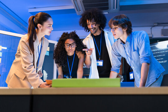 Focused diverse software engineer team analyze computer data on desk. Tech startup developer group discuss program code, web application development, and cyber security system strategy in office.