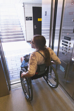Woman with spinal cord injury in a wheelchair using elevator to train access