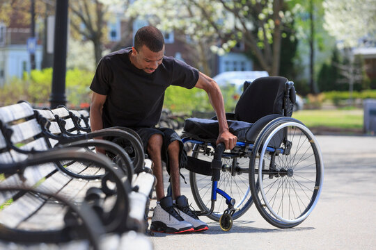Man who had Spinal Meningitis getting out of a park bench and into his wheelchair