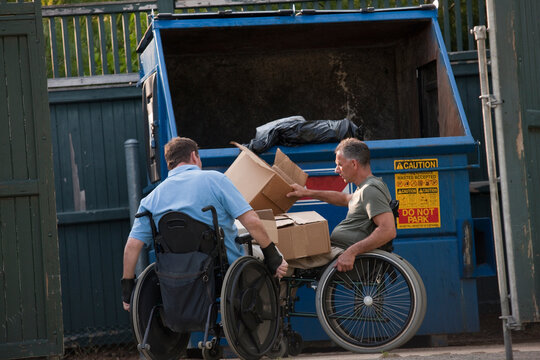 Men in wheelchairs with Spinal Cord Injuries throwing garbage into a trash dumpster