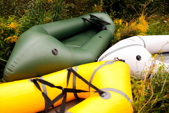 Packrafts and inflatable boats on grassy riverbank top view. Green, yellow and white small light dinghy watercrafts for rafting, adventure tourism, outdoor active lifestyle, kayaking equipment