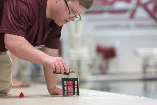 Young man with Down Syndrome working at college testing PH in swimming pool