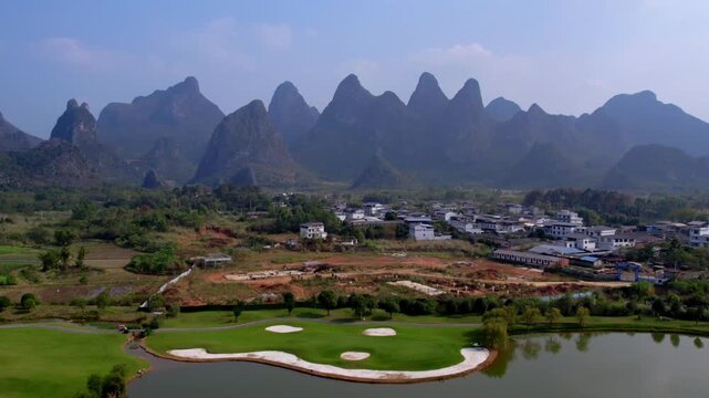 A scenic landscape featuring karst peaks, a golf course with water hazards, and a rural village under clear skies.