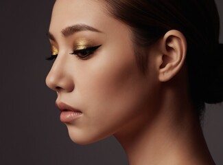 Fototapeta premium Profile of woman with metallic gold eyeshadow and winged eyeliner. Her hair is in a sleek low bun. She has flawless skin and neutral lipstick shade. Pro studio portrait.
