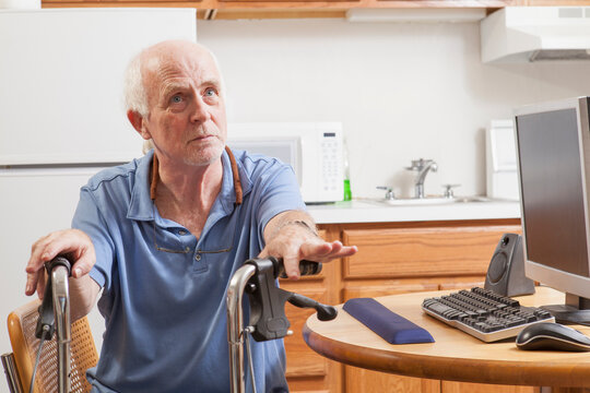 Man with Ataxia holding his walker with his computer in kitchen