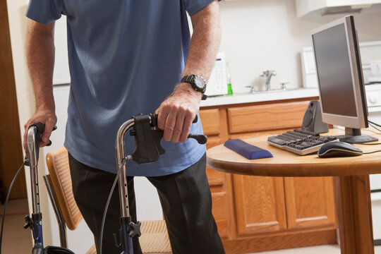 Man with Ataxia holding his walker with his computer in kitchen