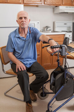 Man with Ataxia holding his walker and sitting at the computer
