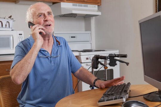 Man with Ataxia talking on his cell phone at the computer in the kitchen