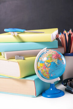 small globe with stack of books and school supplies background