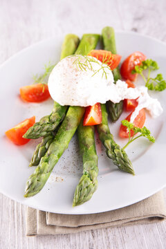 poached egg on green asparagus with fresh tomatoes on plate