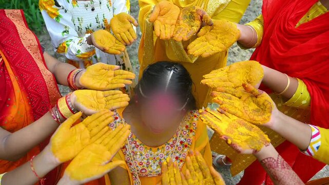 Close-up footage of a traditional Indian Haldi ceremony where family members and friends apply turmeric paste to the bride before marriage. The pre-wedding ritual symbolizes purification, blessings.