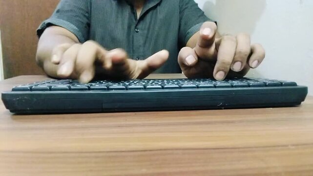 Close up shot of man typing fast on black computer keyboard in bright well lit office room.