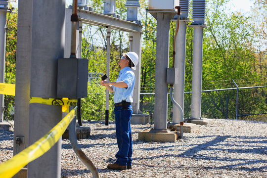 Power engineer using his cell phone at high voltage power distribution station