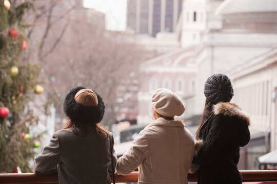 Three women standing on a balcony with Christmas decorations looking out at the city