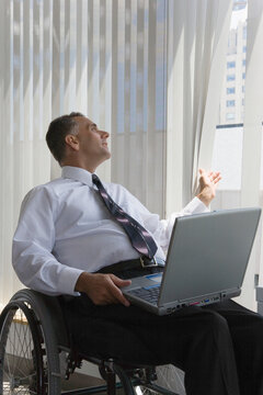 Businessman with a Spinal Cord Injury sitting in a wheelchair with a laptop on his lap