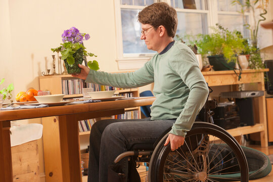 Woman with multiple sclerosis in a wheelchair setting table with flowers for dinner