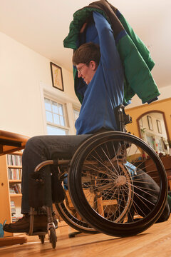 Woman with multiple sclerosis in a wheelchair putting on her coat without help