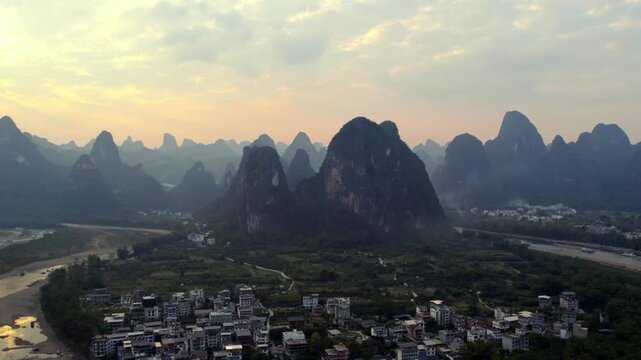A high-angle view of karst peaks, winding rivers, and rural settlements under a soft dawn sky, showcasing a tranquil natural landscape.