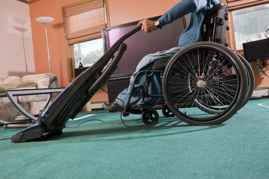 Man with spinal cord injury in a wheelchair using a vacuum cleaner at home
