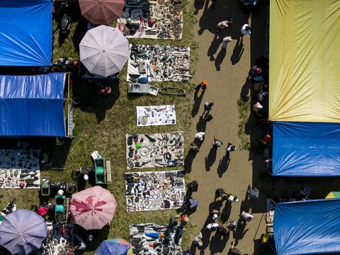 Aerial view of Bonyokan Pasar Legi market with people walking between colorful umbrellas and stalls with goods on the ground in Kecamatan Jatinom, Jawa Tengah, Indonesia.