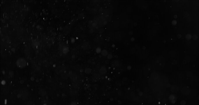 Realistic falling snow and airborne dust particles drifting through dark space. Atmospheric winter storm effect on black background, ideal for overlays, VFX compositing and cinematic scenes.