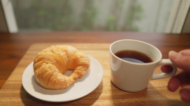 For morning coffee, a wooden tray framed with a cup of freshly brewed coffee and a croissant serves as a refreshing breakfast, perfect for enjoying a sip.