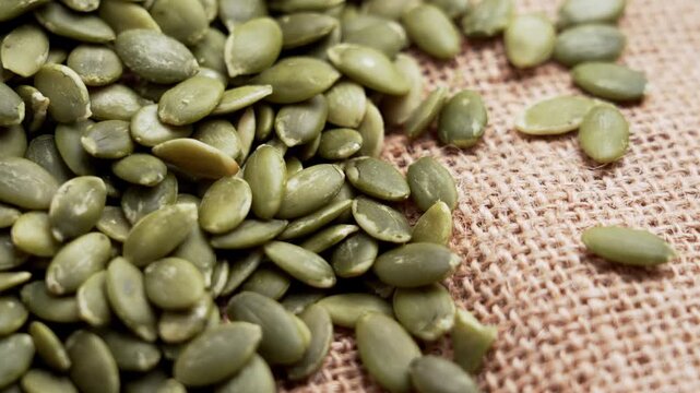 Close up of hulled pumpkin seeds (pepitas) scattered on natural burlap fabric. Dietary fiber superfood. Rotation