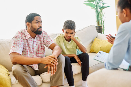 Father with his teenage son boy at meeting with social worker, psychologist discussing mental health family sitting on sofa in psychotherapist office