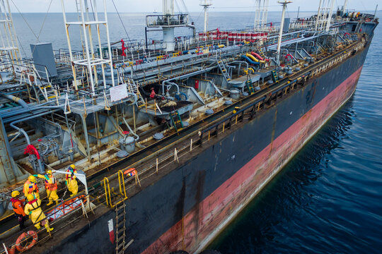 Aerial view of a large industrial tanker ship with workers in yellow safety suits on the deck surrounded by complex piping at sea Indonesia.