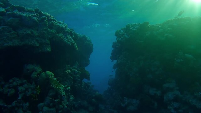 Approaching a break in the coral reef wall leading to the open sea in the evening light. Crack in the reef under bright sun rays at sunset, backlit. A passage in the coral wall in the sunlight
