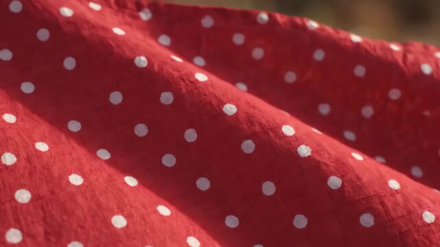 Cinematic close up of vintage red fabric with white polka dots moving smoothly in a gentle breeze across the frame