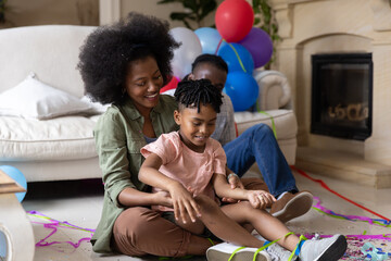 Obraz premium African American mother and son sitting on floor in living room holding ribbons, balloons, confetti
