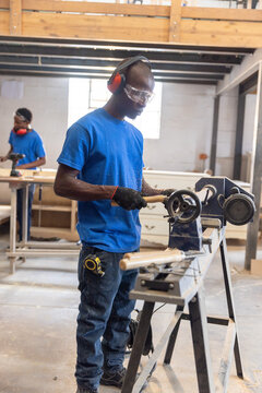 Wood lathe shaping wooden spindle on metal stand in carpentry workshop, sawdust dusting floor
