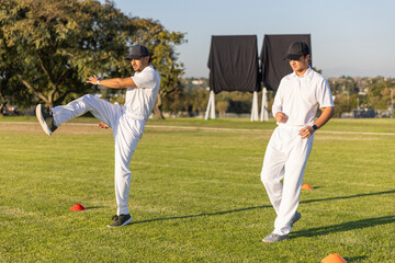 Obraz premium Diverse men training bowling and walking in white kits on pitch with orange cones, sight screens