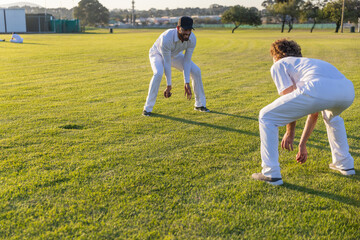 Obraz premium Two male cricketers practicing on grassy outfield in white clothing with dark cap near nets