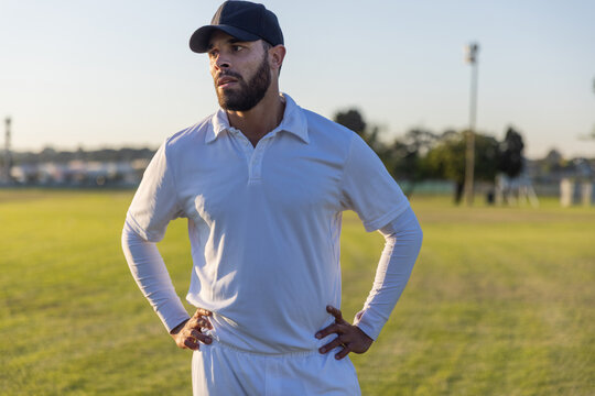 Mid adult male standing on grassy sports field wearing white cricket uniform and black cap